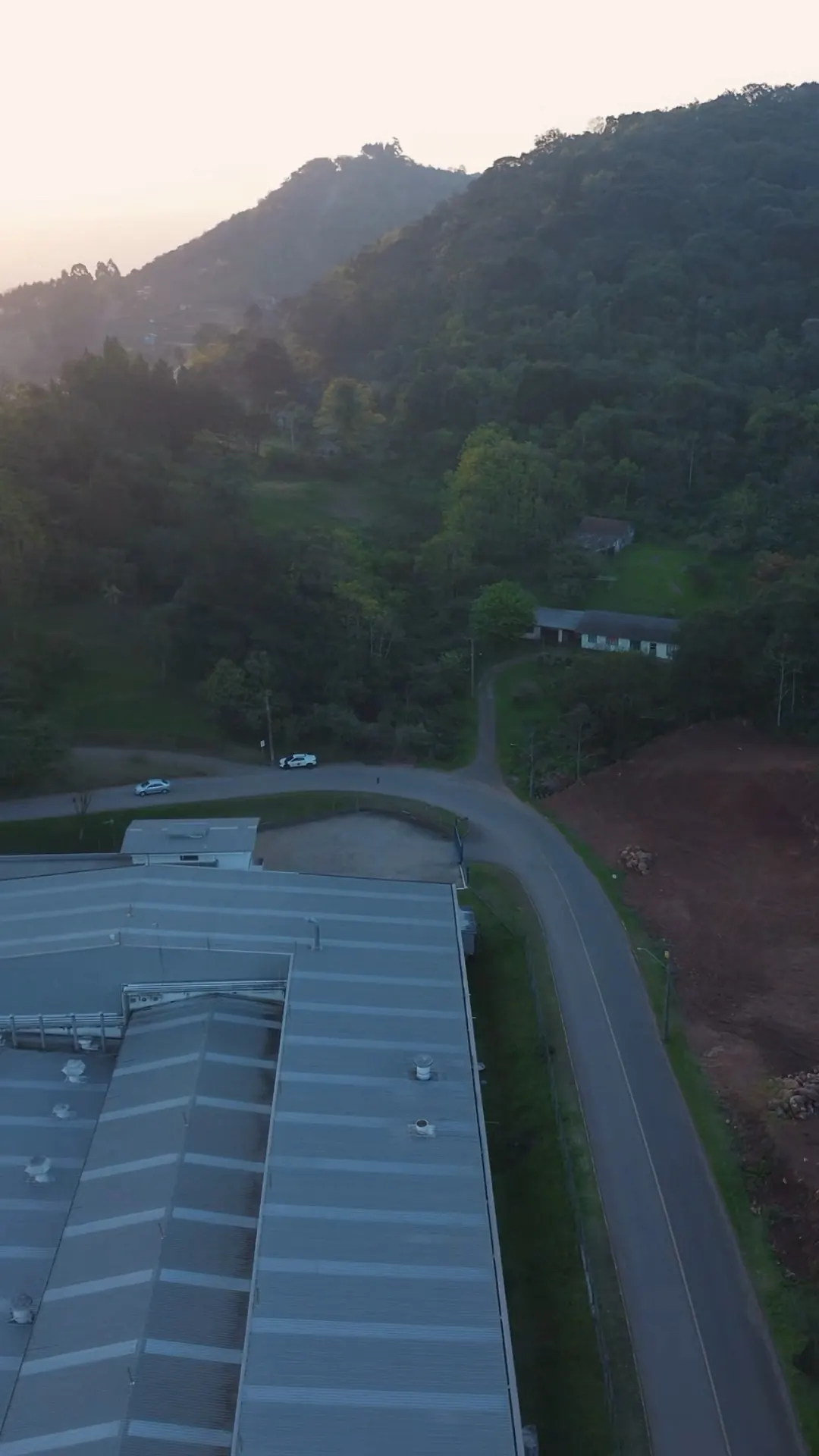 A rua asfaltada em curva que passa ao lado do terreno, com o pavilhão industrial à esquerda.