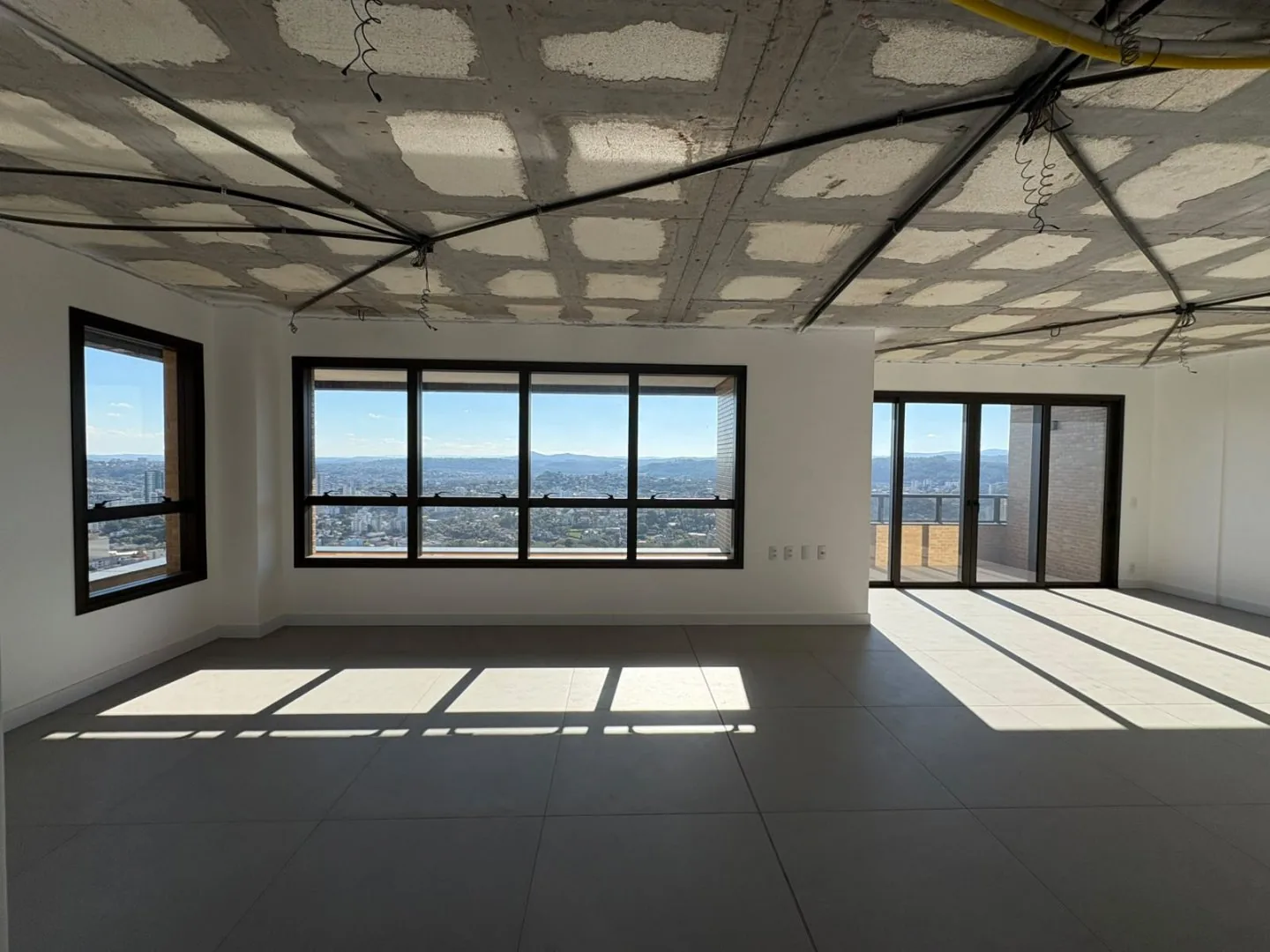 Sala em fase de acabamento, teto sem forro, janelas e saída para a sacada.