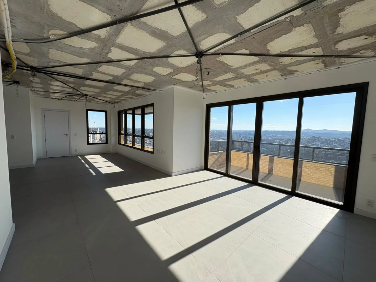 Ambiente integrado em obra, com porta de vidro para a sacada e vista da cidade.