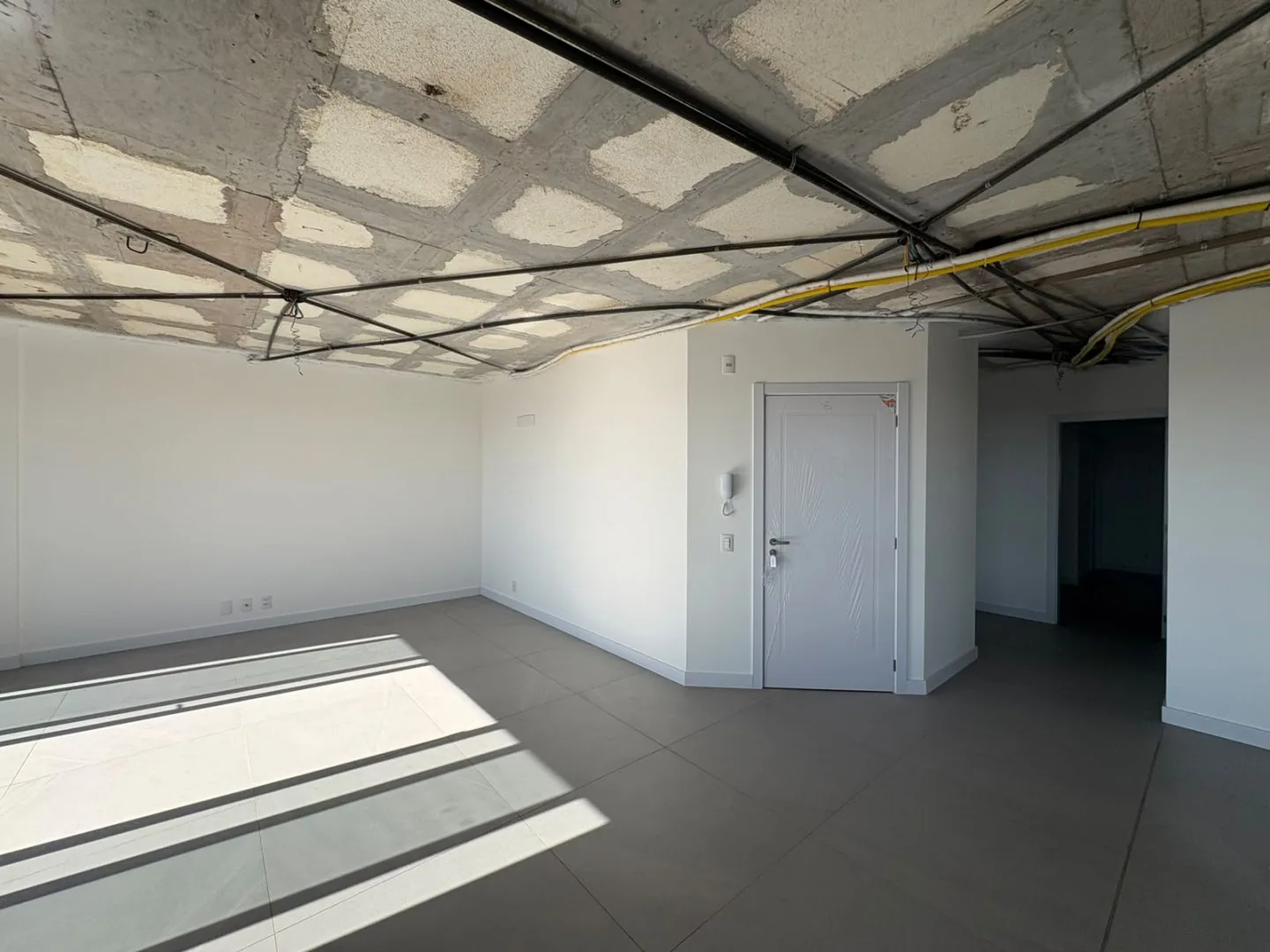 Ambiente vazio em obra, com porta de entrada e corredor ao fundo.