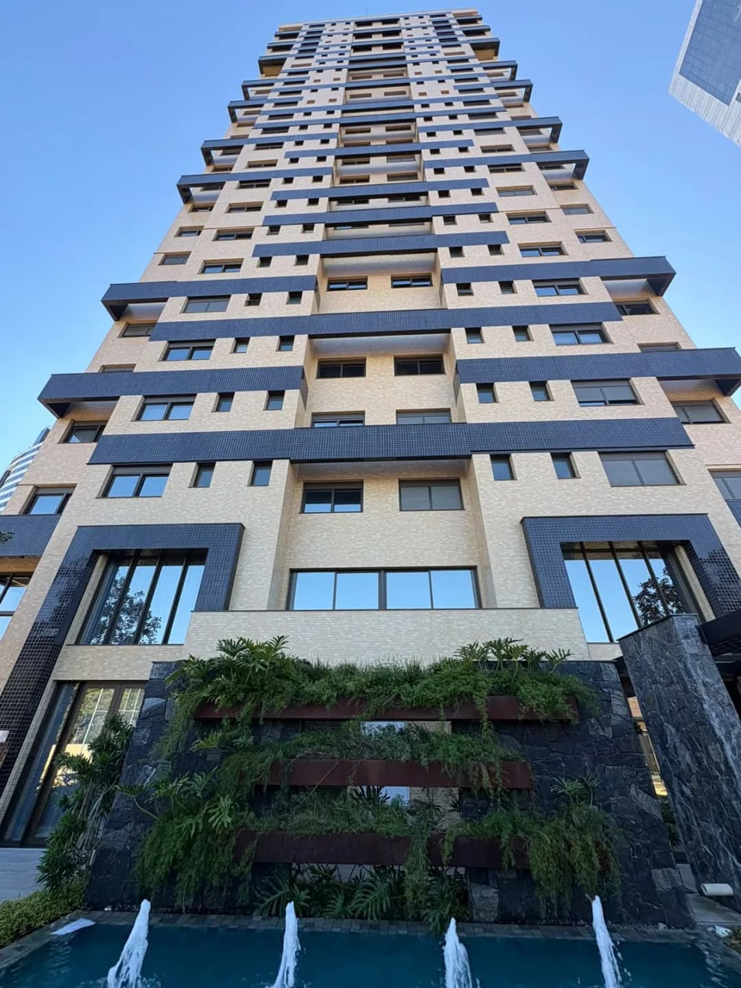 Fachada da torre vista de baixo, com jardim vertical e espelho d'água.