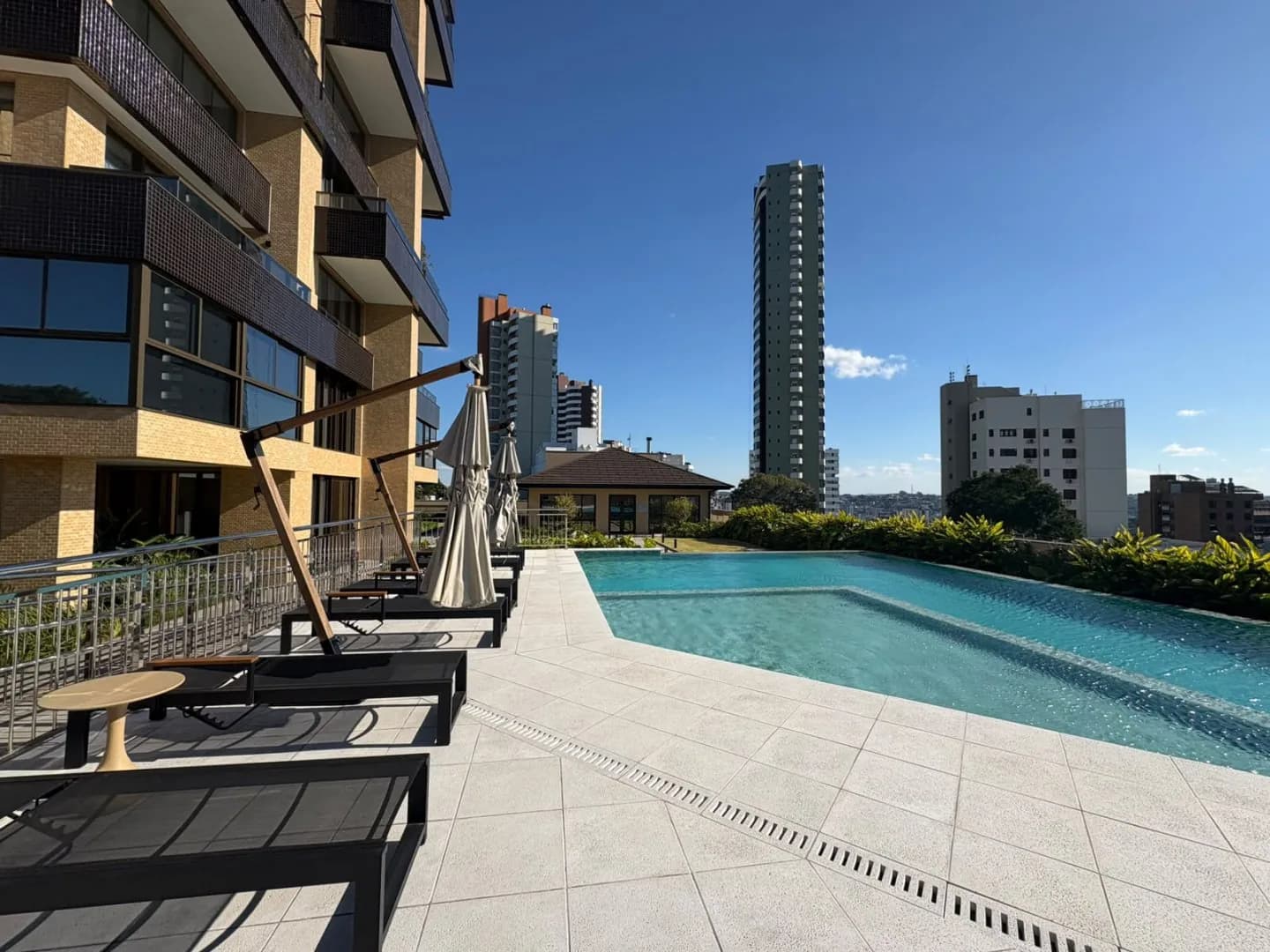 Piscina ao lado da torre, com espreguiçadeiras e guarda-sóis fechados.