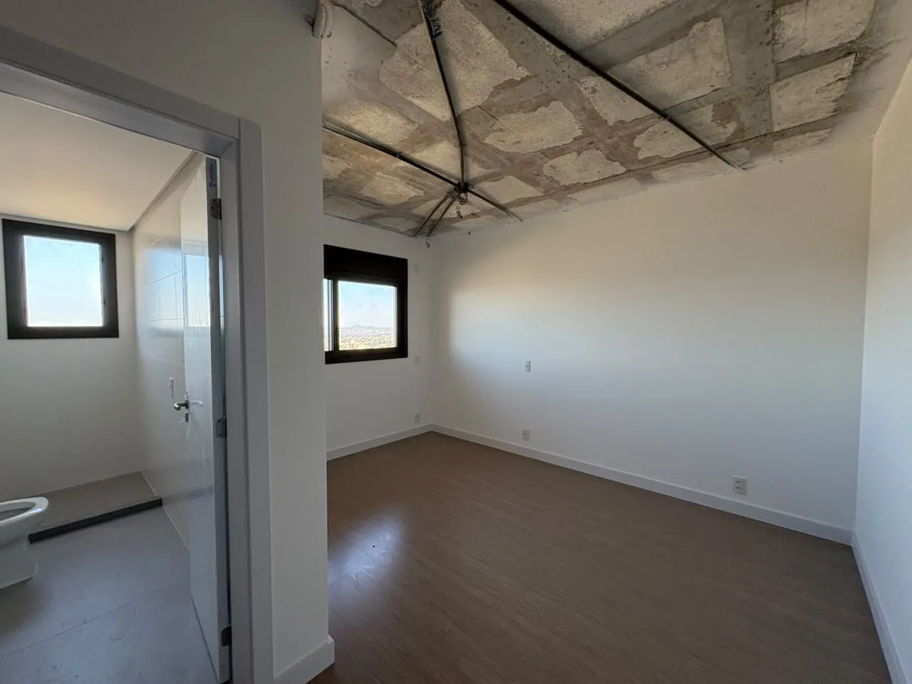 Suíte em acabamento, com piso vinílico e banheiro ao lado.
