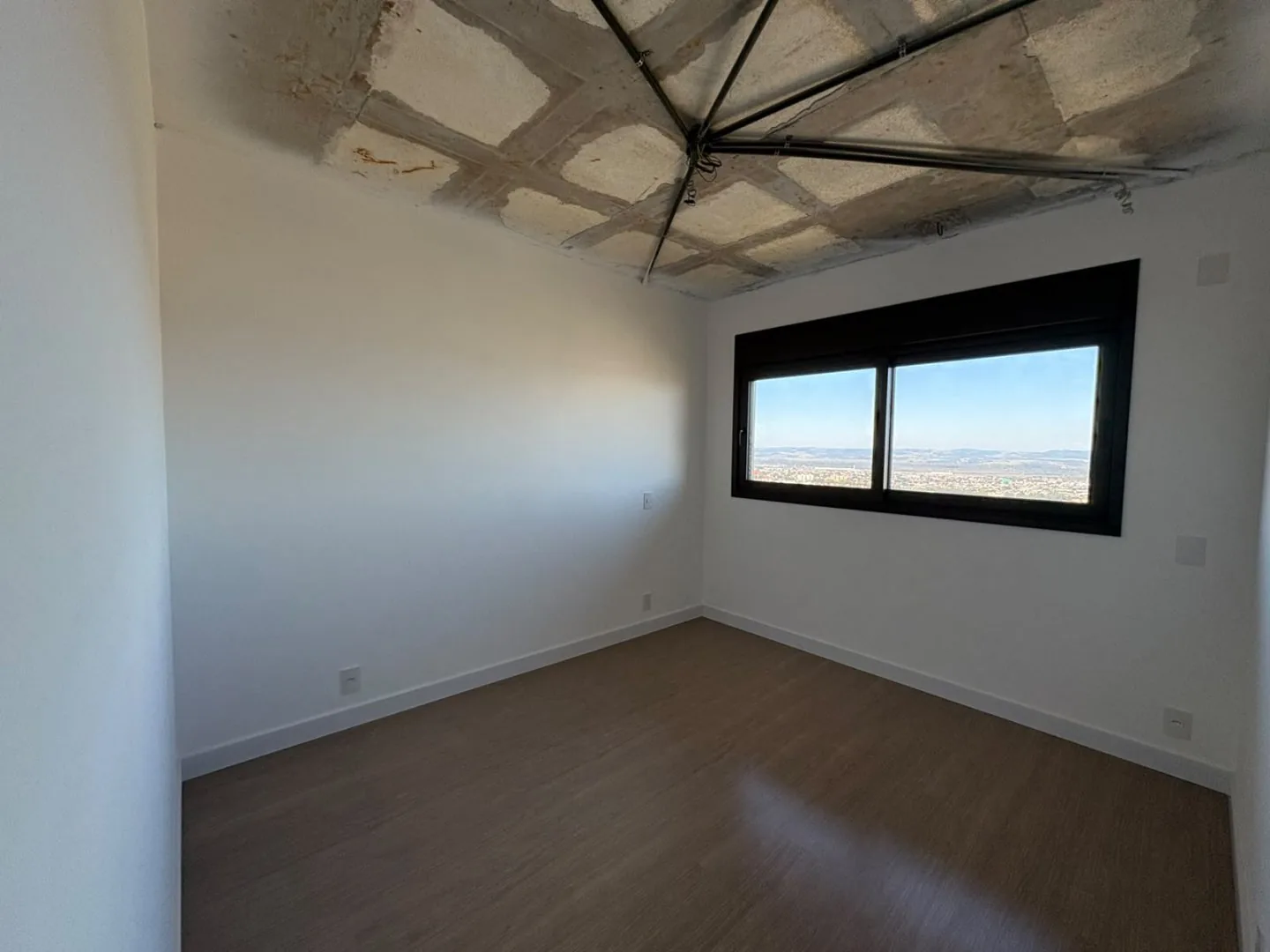 Dormitório com piso vinílico e janela voltada para a cidade.