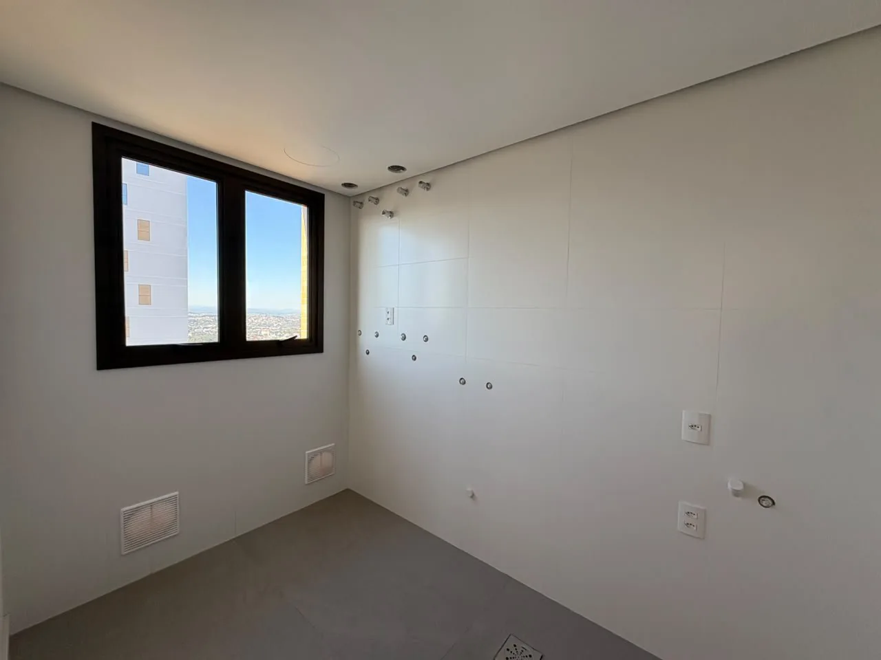Banheiro em acabamento, com revestimento branco e pontos de hidráulica.
