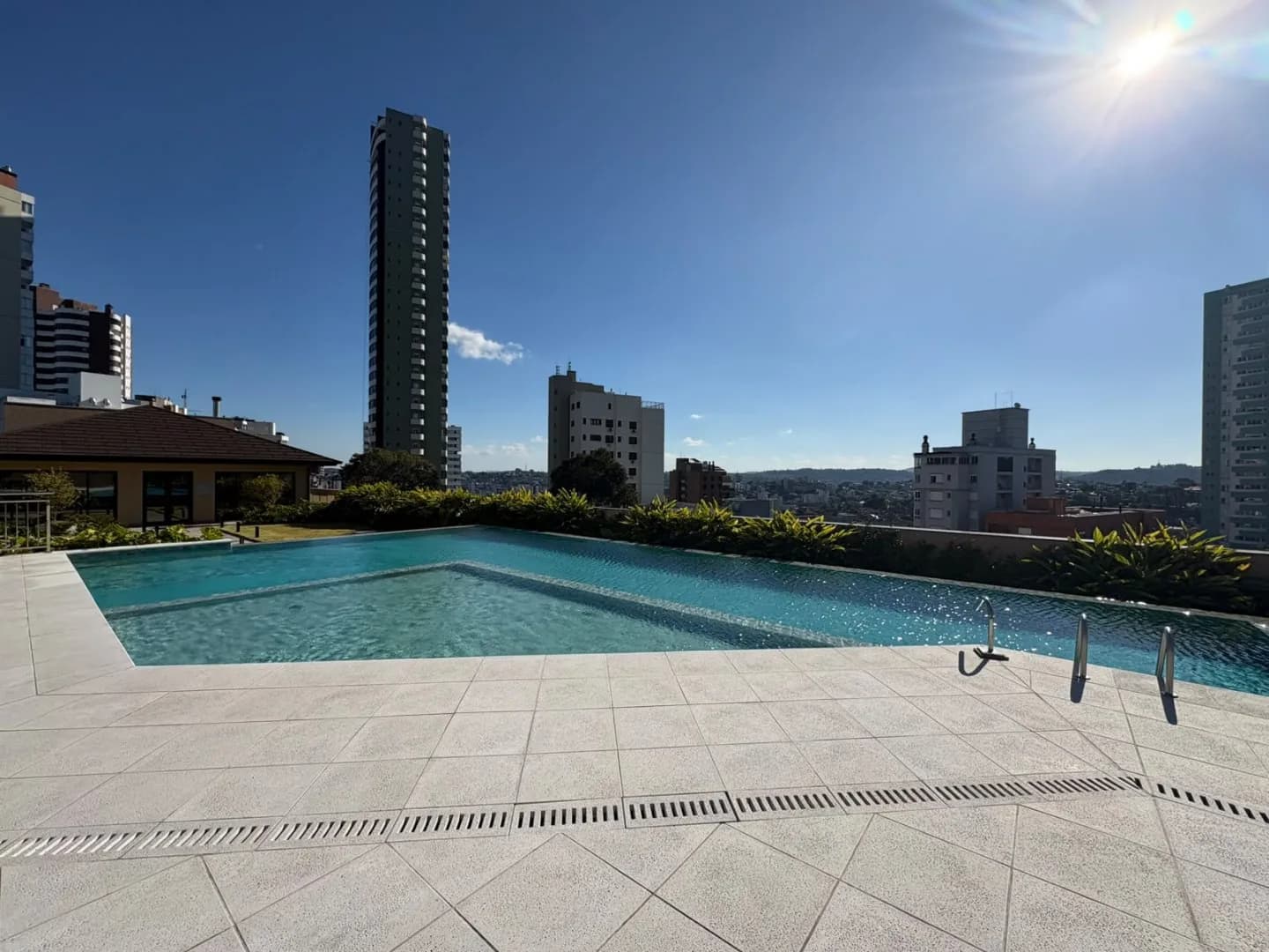 Piscina com borda infinita no terraço, com deck e vista da cidade.