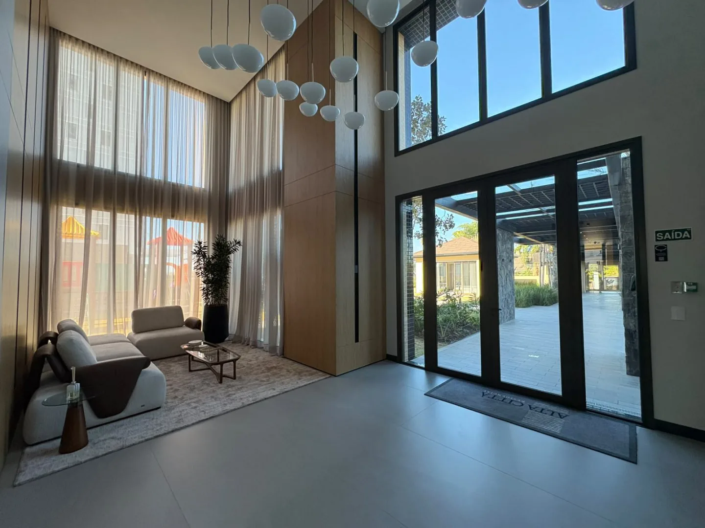 Hall de entrada com pé-direito alto, sofás e porta de vidro para o pátio.