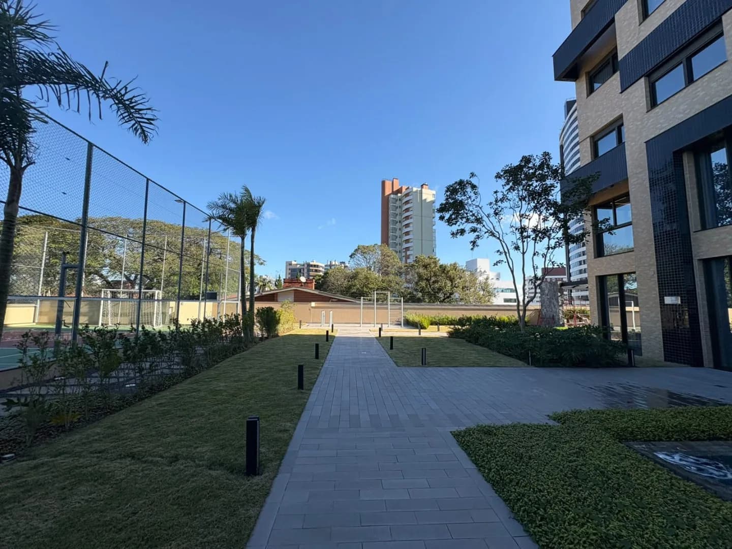 Caminho de pedra entre os gramados, com a quadra cercada à esquerda.