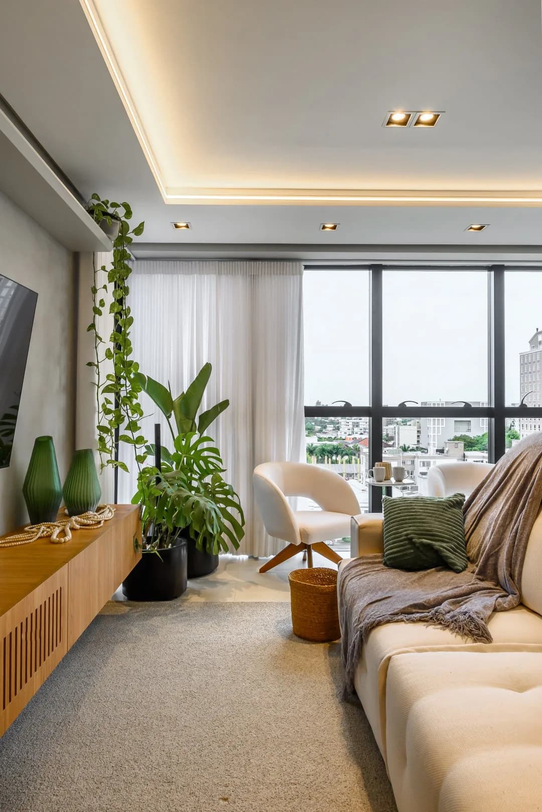 Sala de estar com sofá claro e plantas junto à janela.