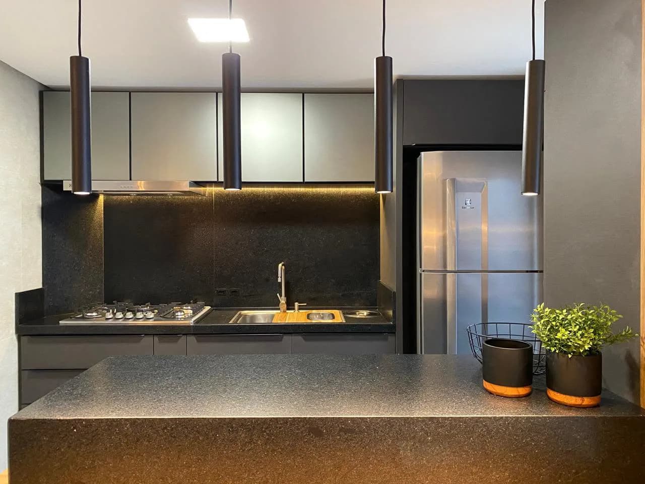 Cozinha com bancada escura e armários pretos.