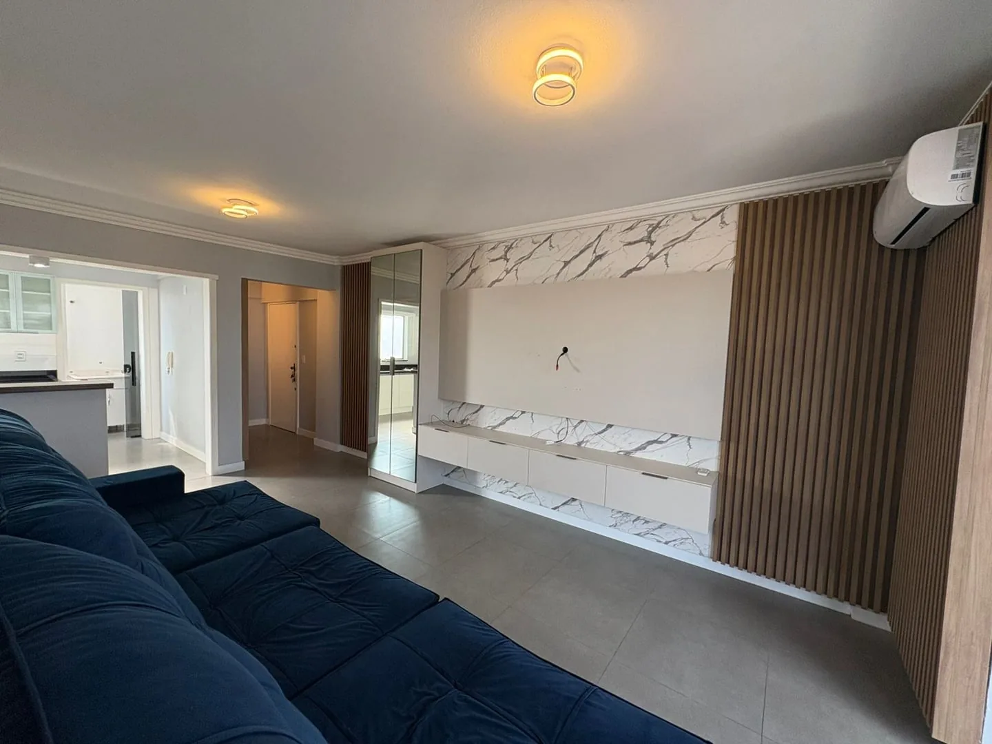 Sala com ar-condicionado split, painel ripado e entrada do apartamento ao fundo.