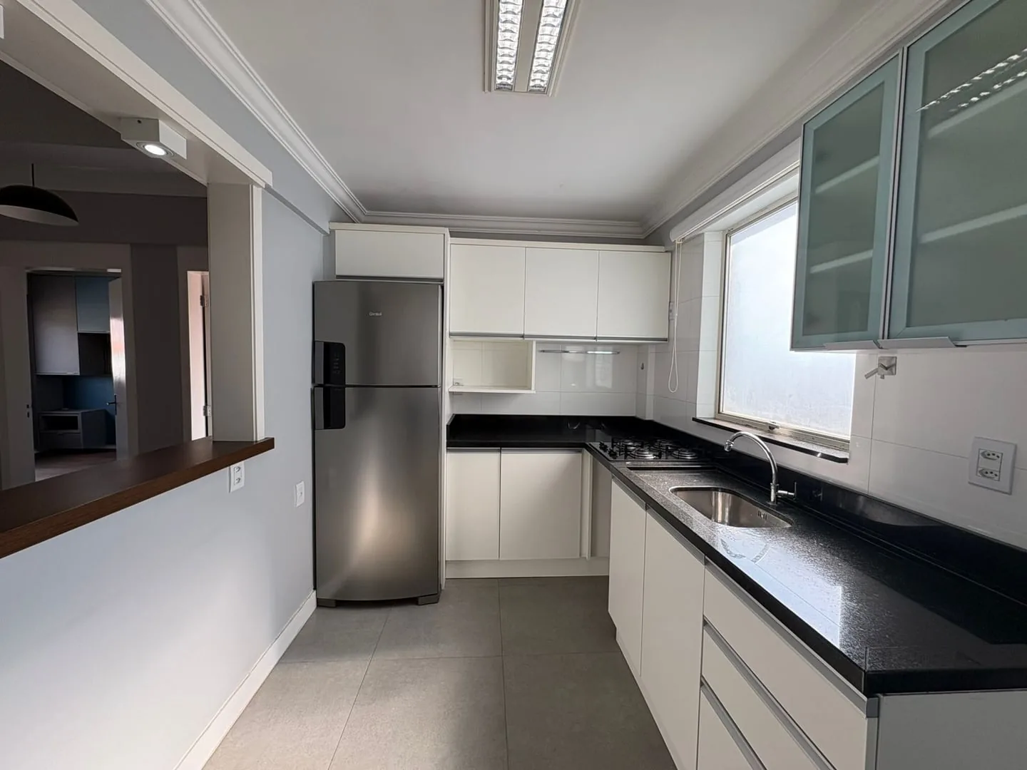 Cozinha em L com bancada preta, cooktop e armários brancos.