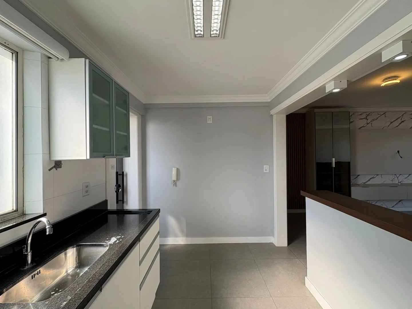 Cozinha com pia de inox, bancada preta e passa-pratos para a sala.