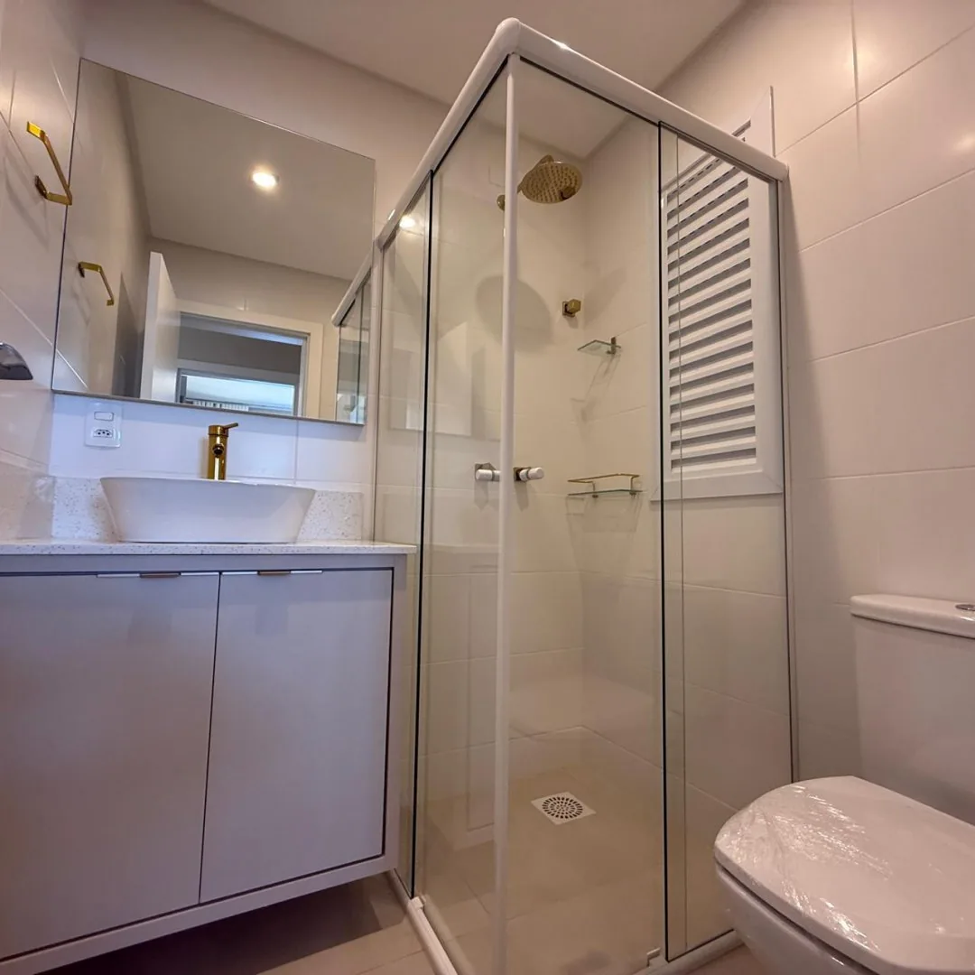 Banheiro com box de vidro e bancada clara.