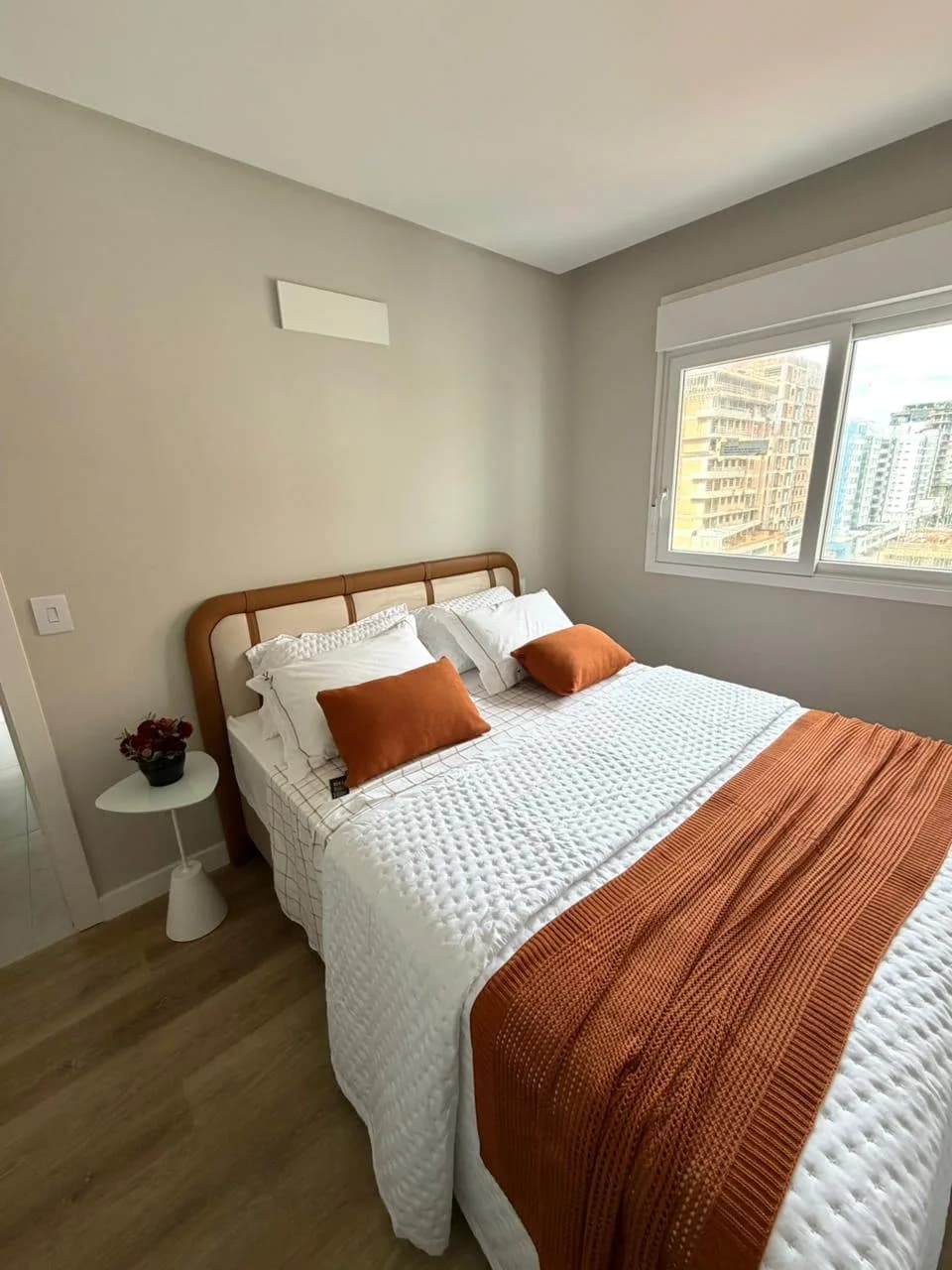 Dormitório com cama de casal, vista para os prédios vizinhos
