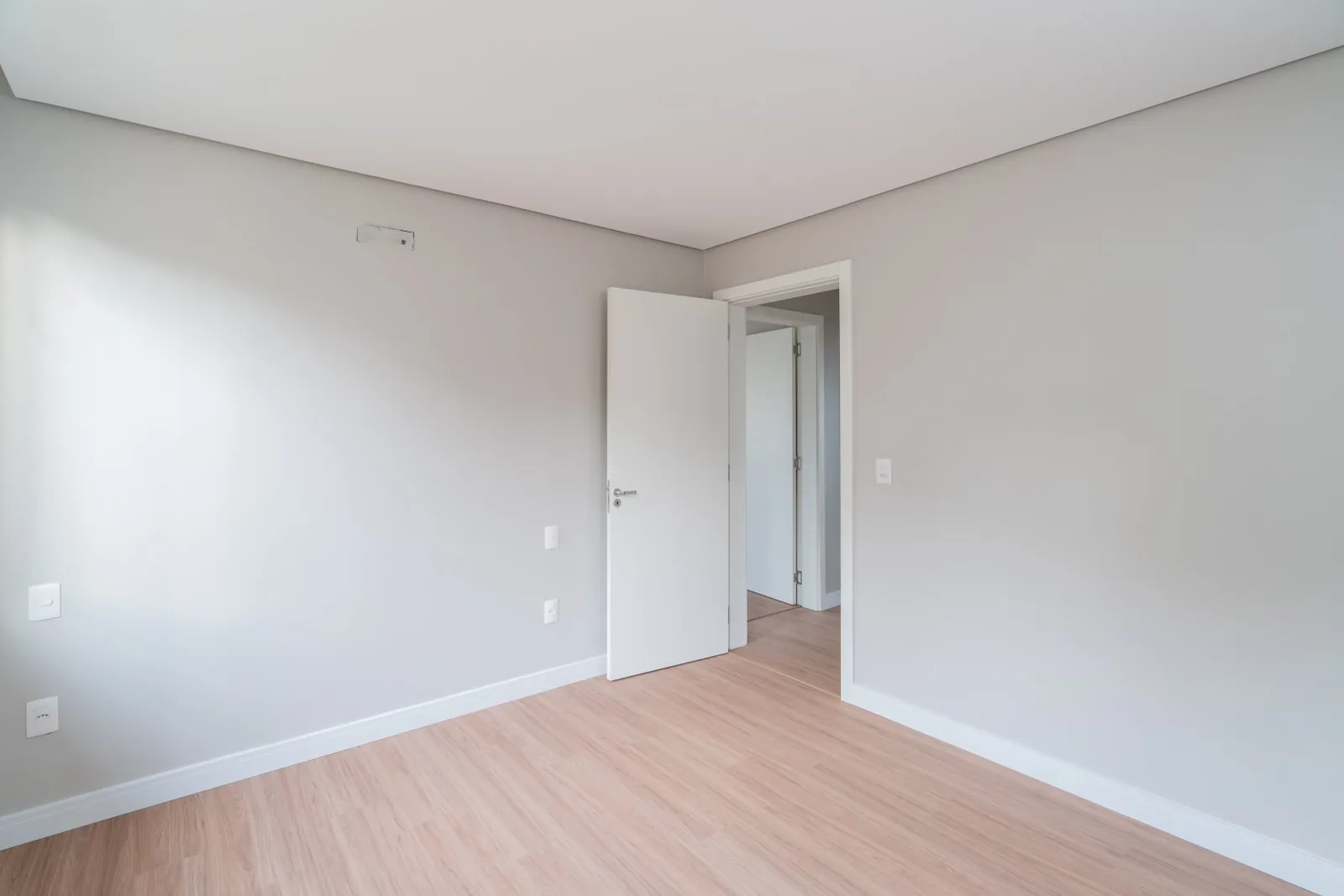 Quarto vazio com piso laminado e porta aberta para o corredor.