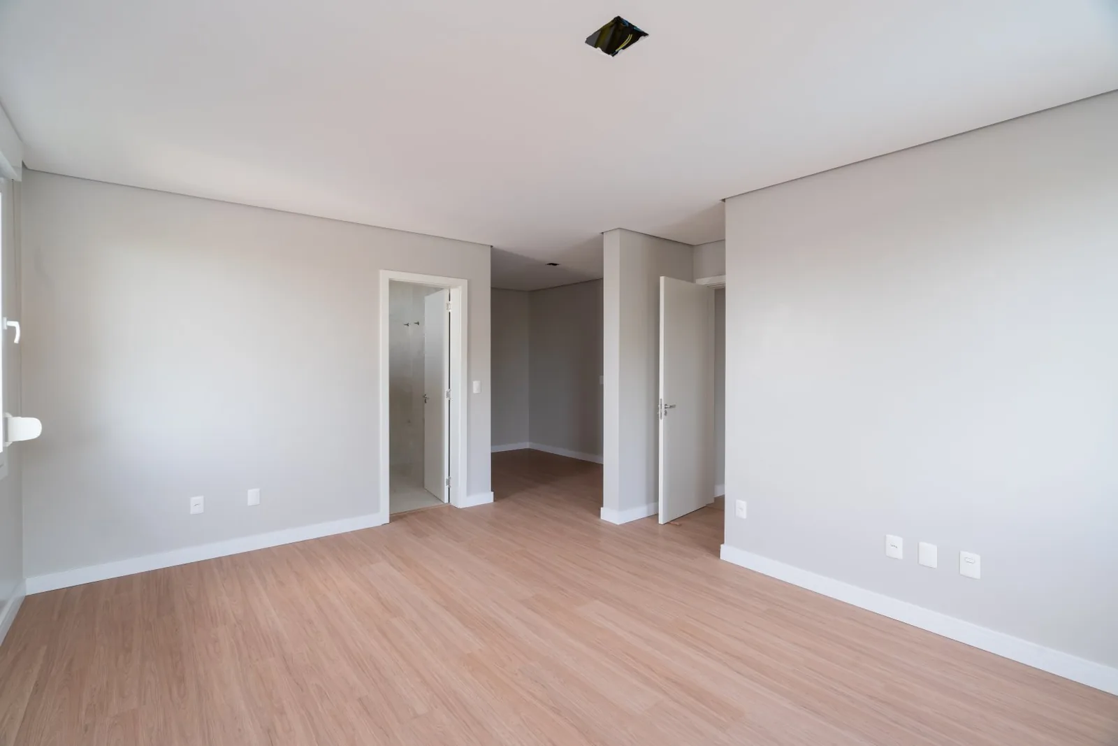 Suíte vazia com piso laminado, porta do banheiro e acesso ao closet.
