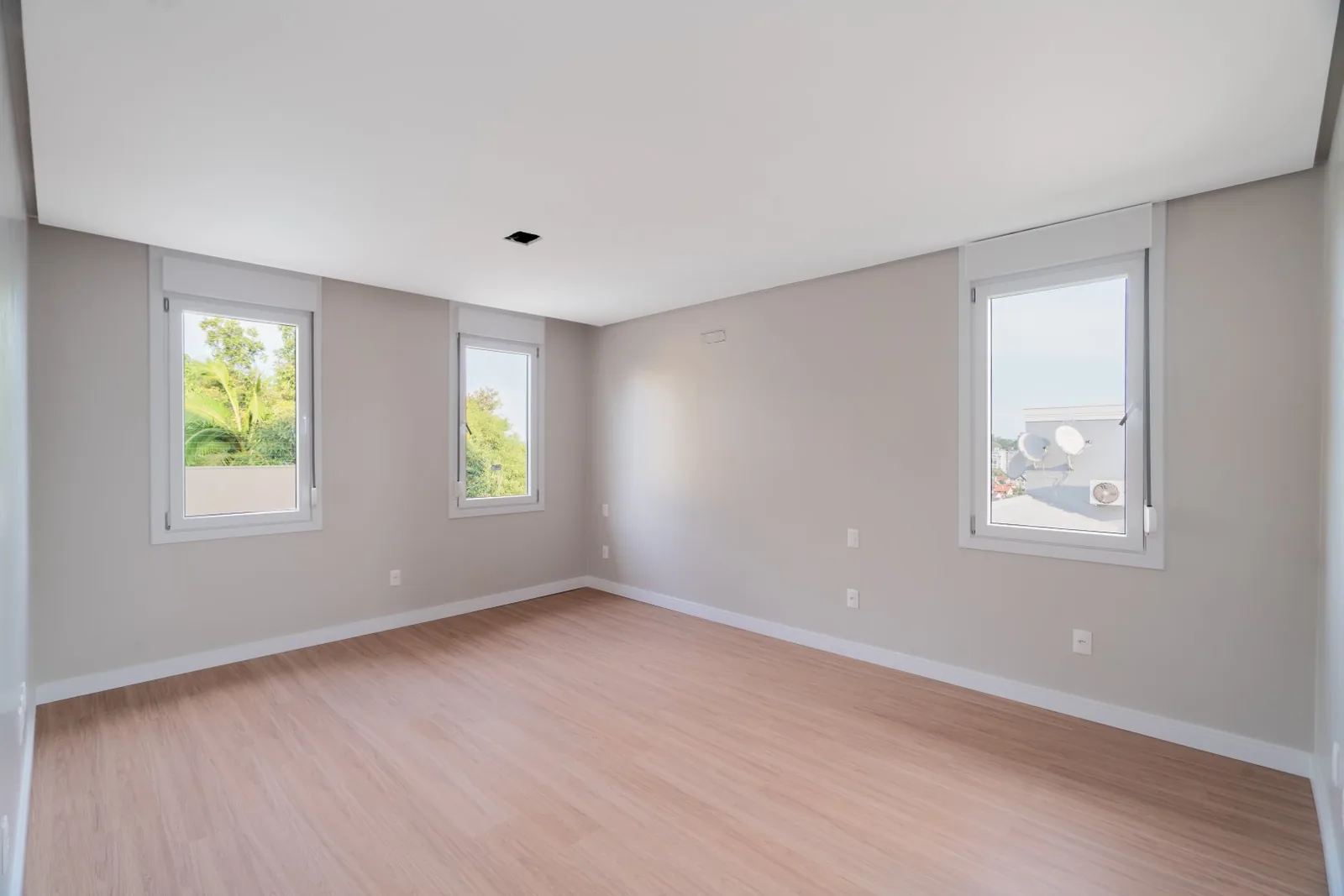 Quarto vazio com três janelas e piso laminado.