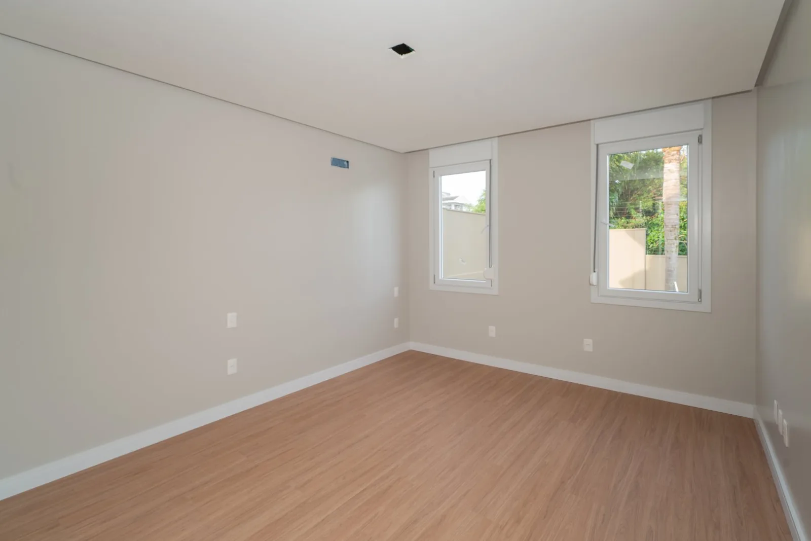 Quarto vazio com duas janelas e piso laminado.