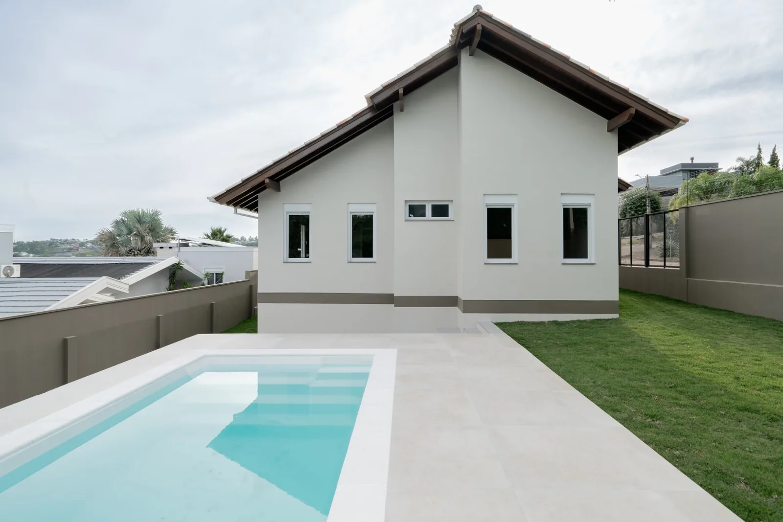 Piscina com deck claro e fachada lateral dos quartos ao fundo.