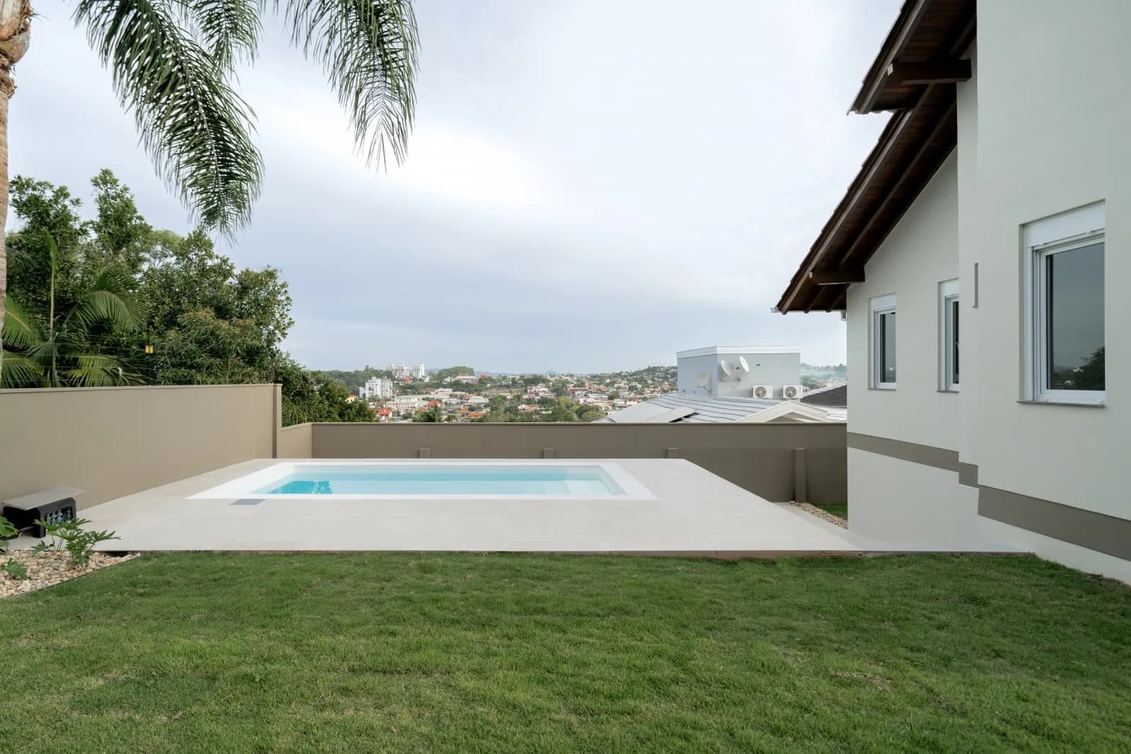 Piscina vista do gramado, com a cidade ao fundo.