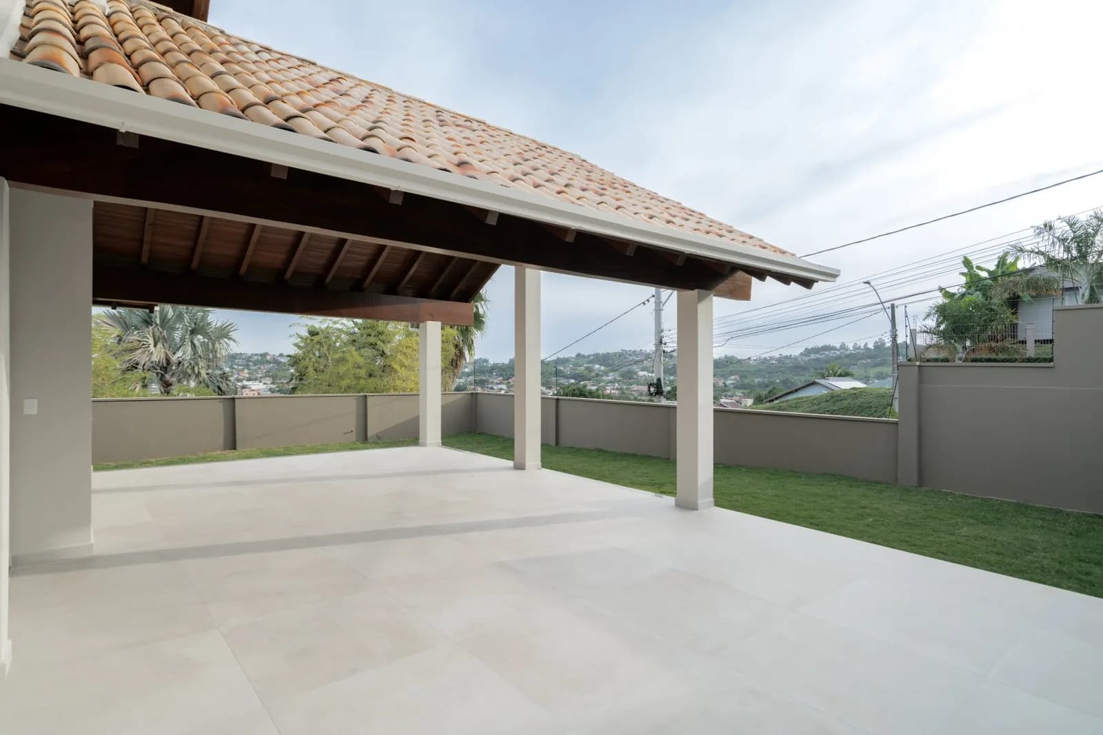 Varanda coberta em porcelanato com gramado e vista ao fundo.