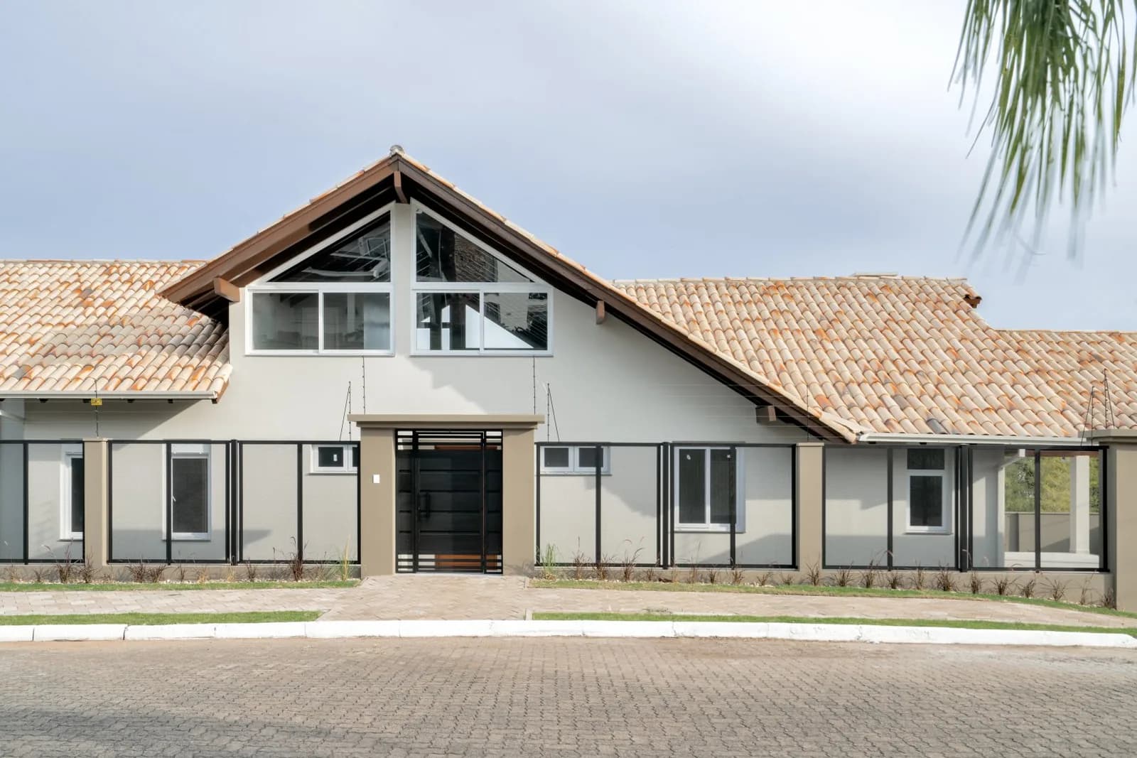 Fachada frontal centrada com portão preto e mezanino de vidro.