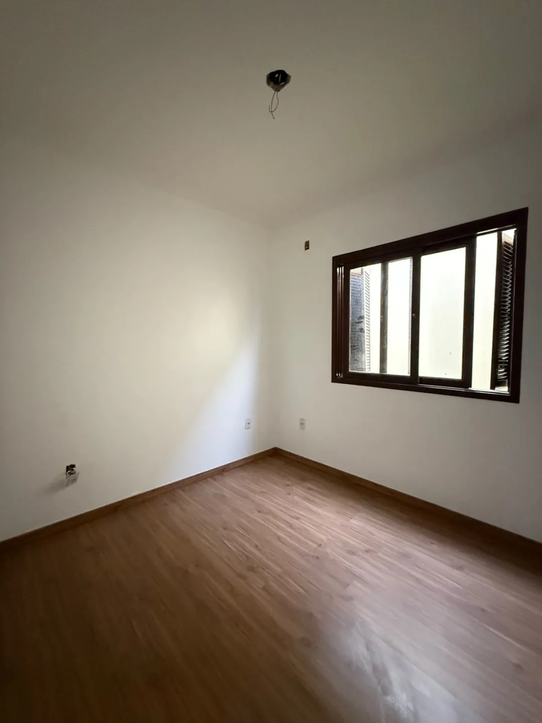 Dormitório vazio com piso laminado e janela de madeira.