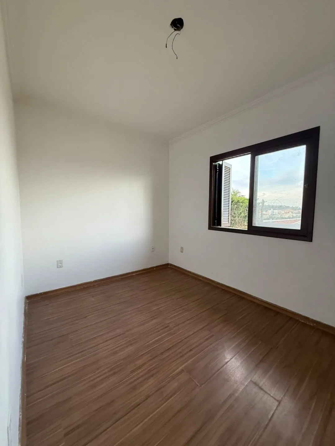 Dormitório vazio com piso laminado e janela com vista para fora.