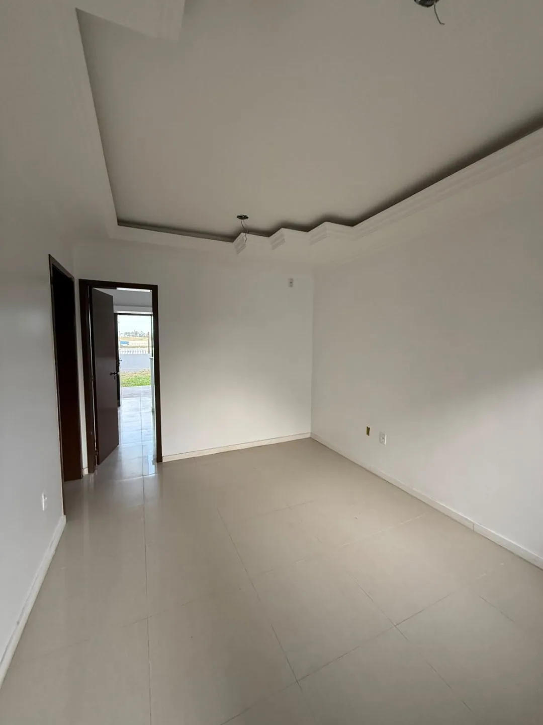 Sala vazia com piso claro, sanca de gesso e porta aberta para o pátio.
