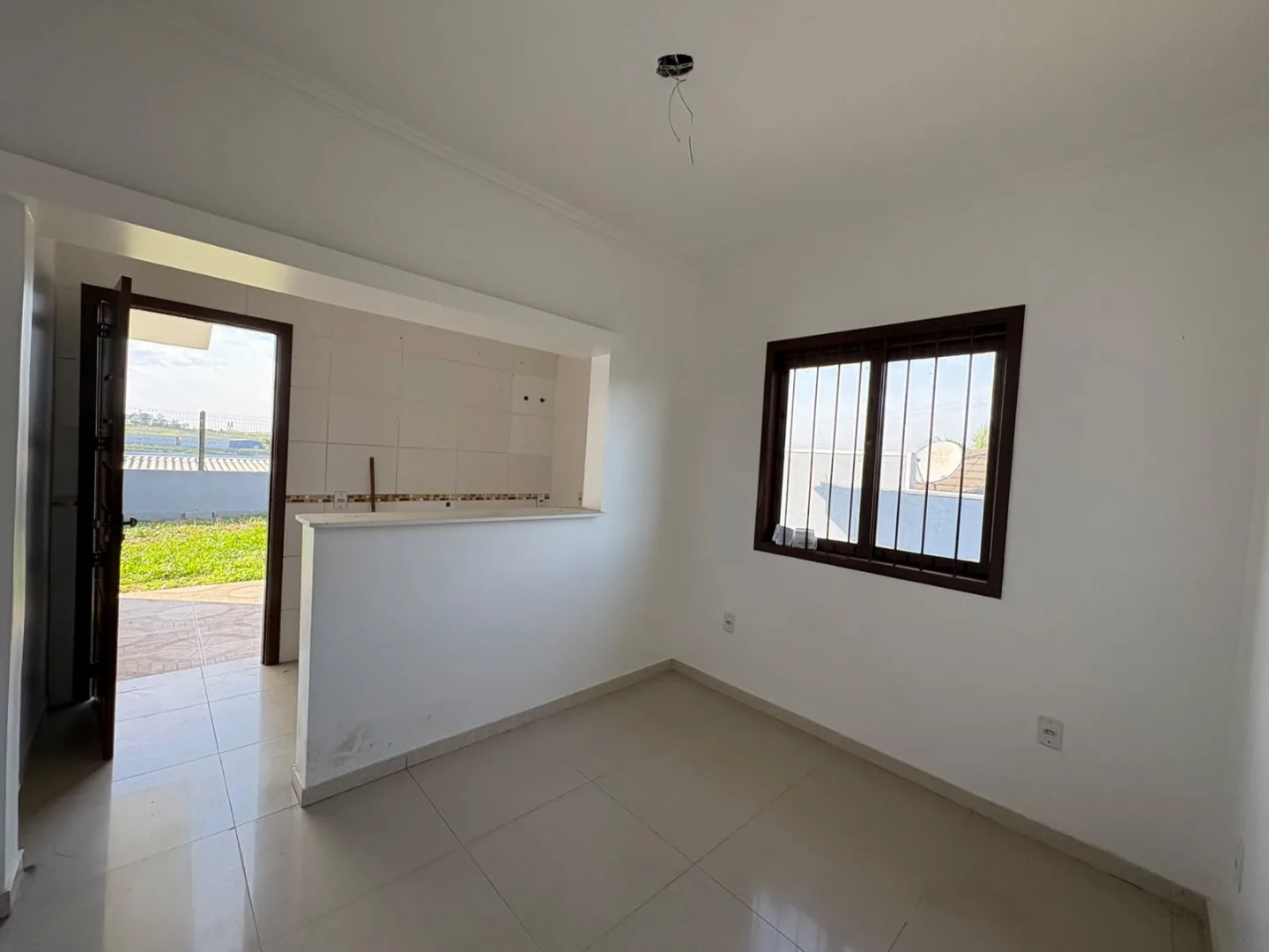 Sala com balcão da cozinha em alvenaria, janela e porta aberta para fora.