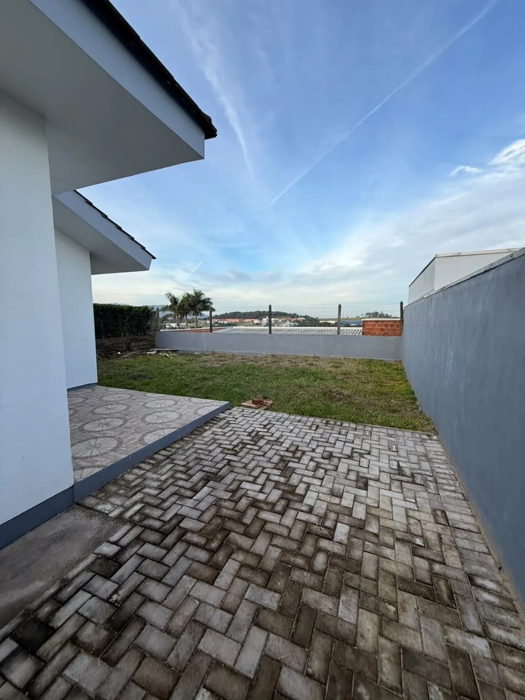 Pátio lateral com piso de paver, gramado e muro que cerca o terreno.