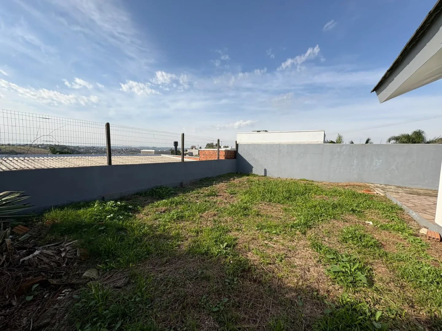 Área gramada dos fundos, cercada por muro e tela, com vista aberta.