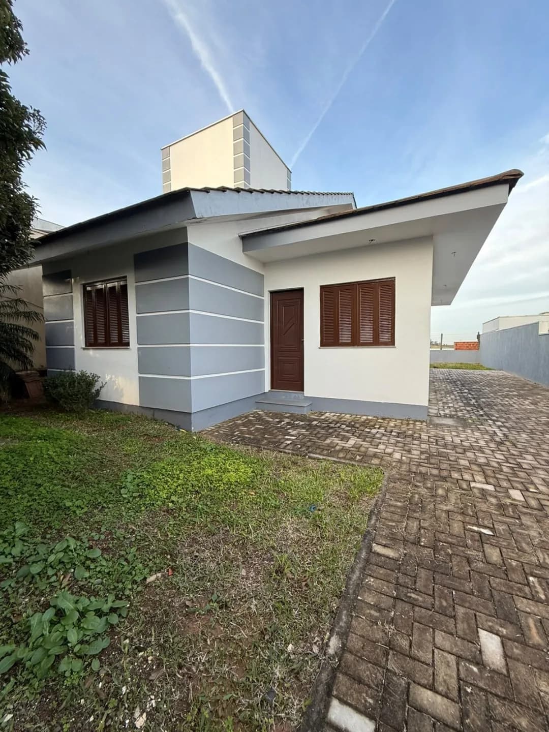 Fachada da casa térrea com porta de entrada, janela de madeira e calçada de paver.