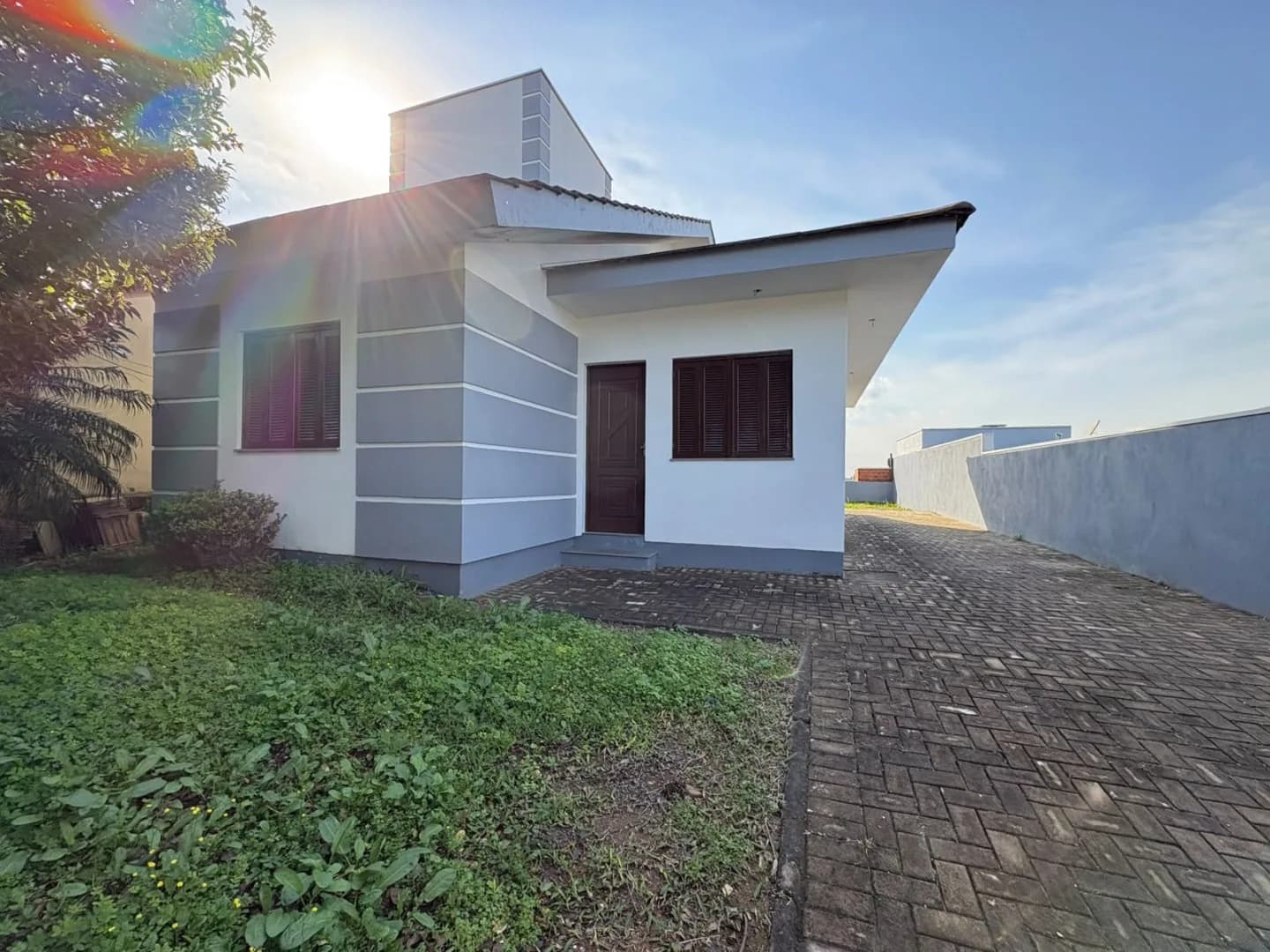 Frente da casa com porta de entrada, janela e acesso calçado ao lado.
