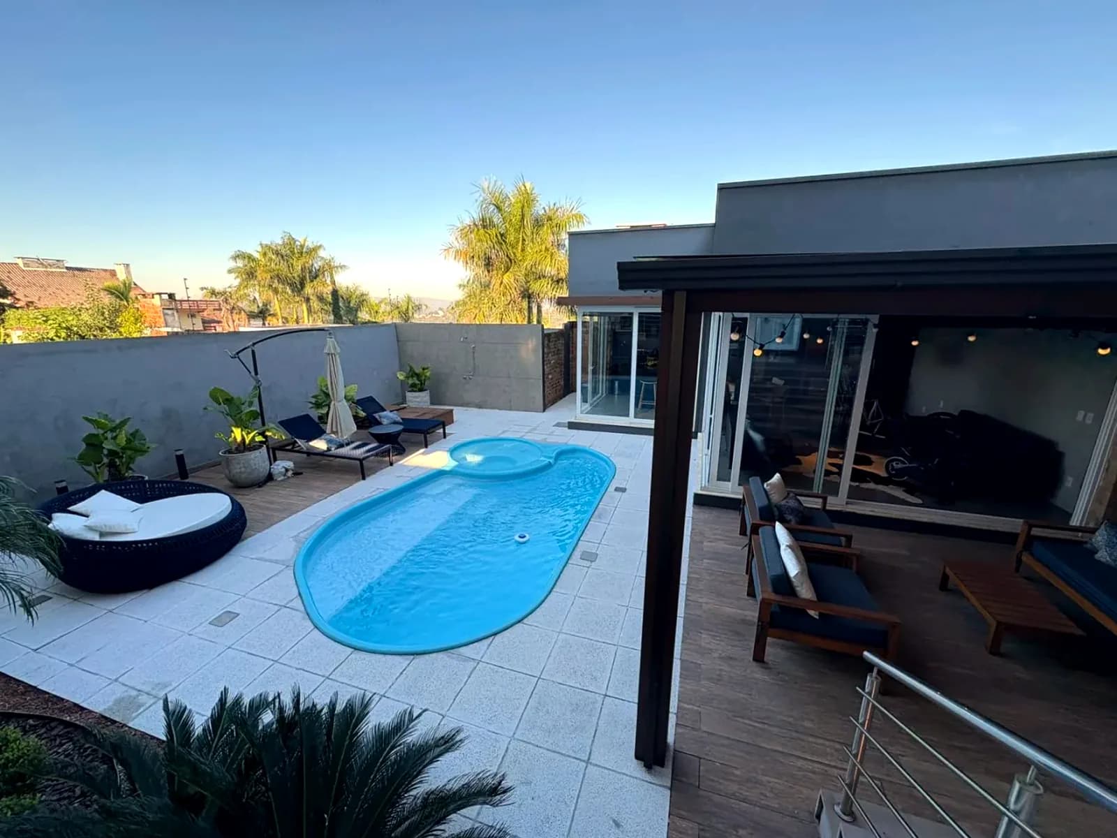 A casa contemporânea vista do pátio, com a piscina em primeiro plano e palmeiras ao fundo.