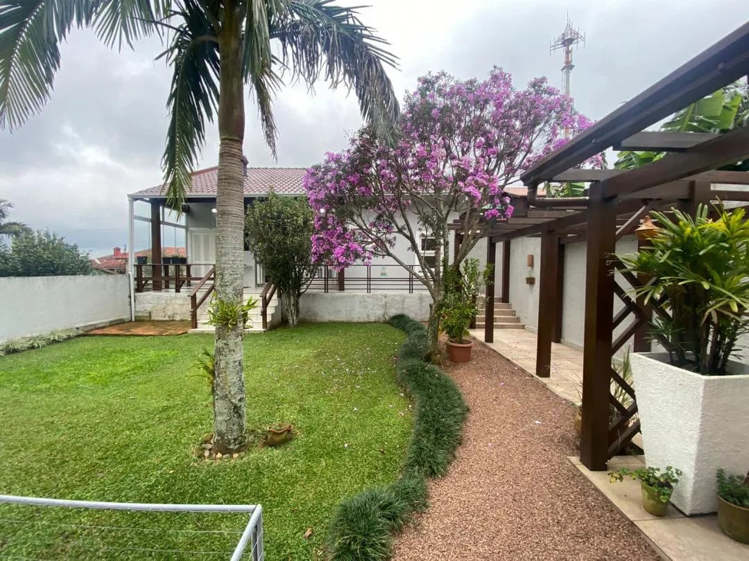 Piscina no pátio de lajota, com a casa térrea e a varanda coberta ao fundo.
