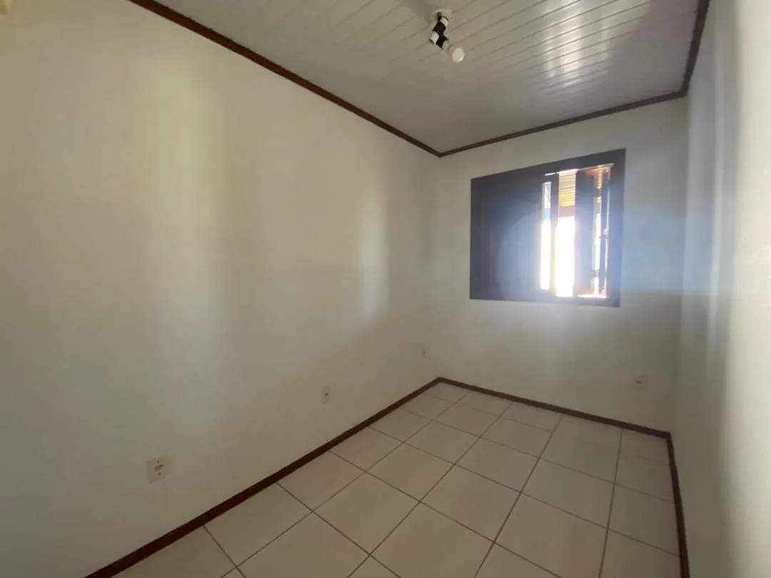 Dormitório vazio com janela de veneziana e piso cerâmico branco.