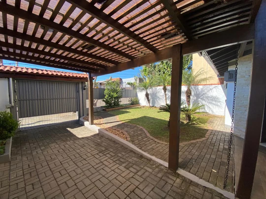 Pergolado de madeira, pátio calçado e portão de garagem ao fundo.