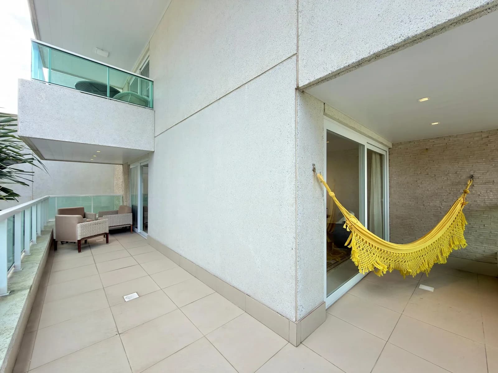 Sacada frente e lateral do apartamento, com rede e vista para os prédios vizinhos.