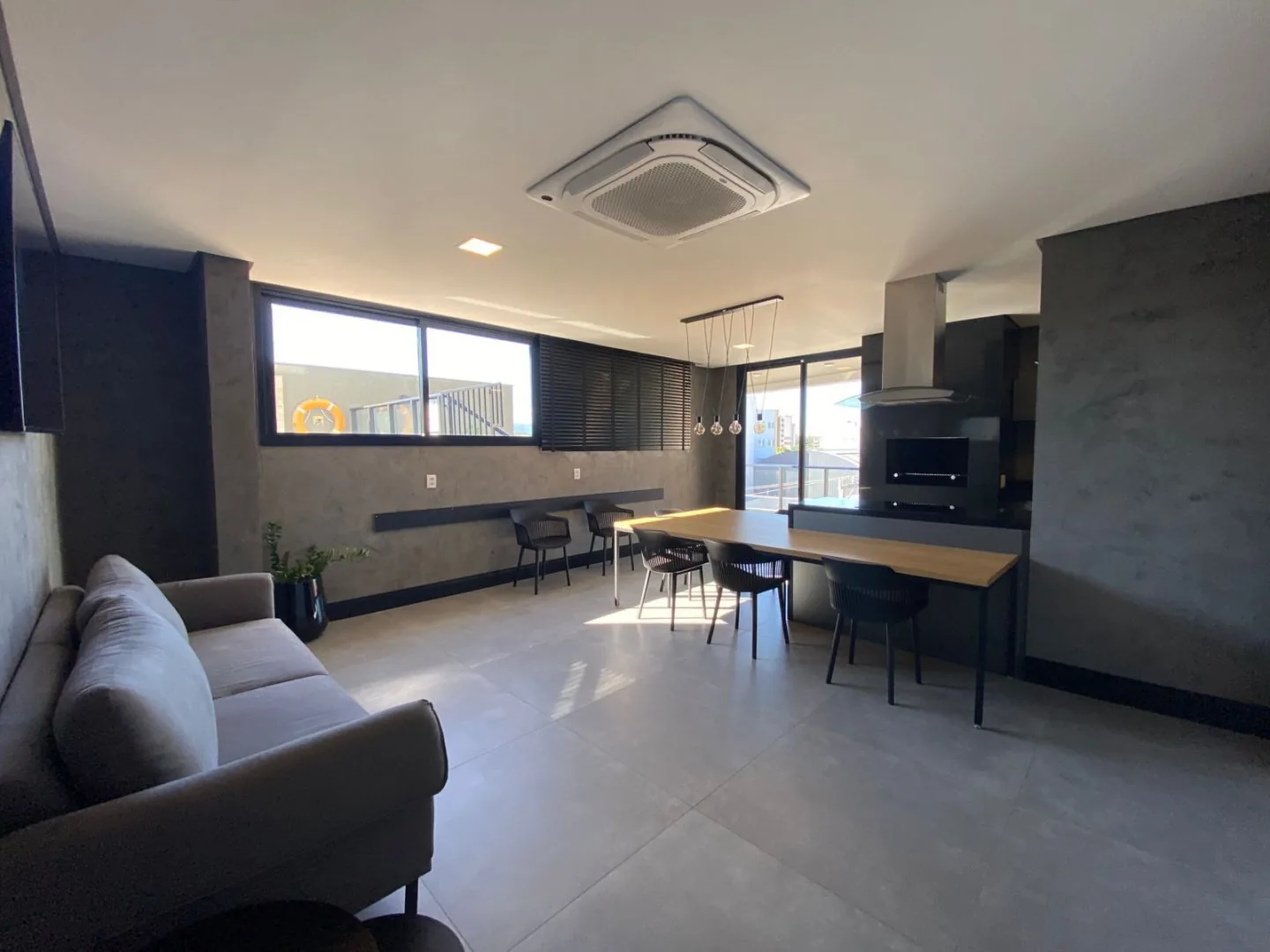 Salão de festas com mesa comprida e cozinha de apoio.