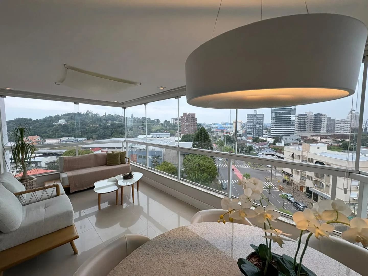 Sacada envidraçada com mesa e vista aberta da cidade.