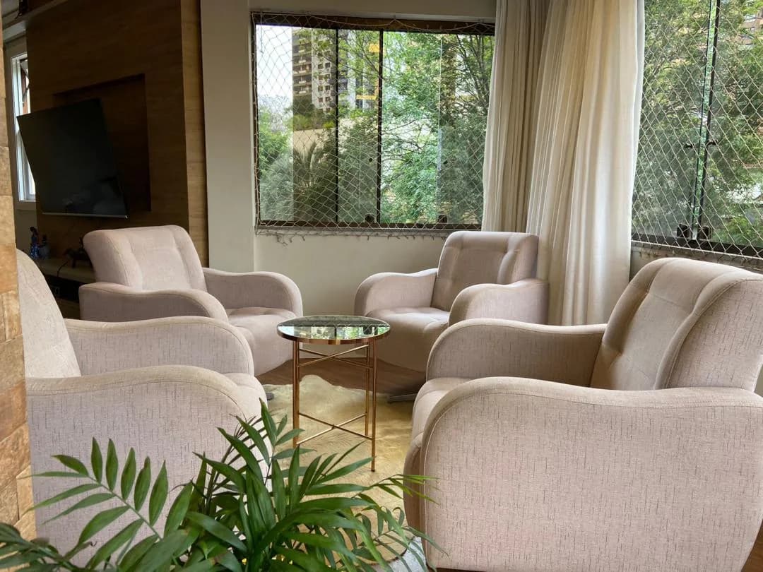 Estar com poltronas claras e janela para o arvoredo.