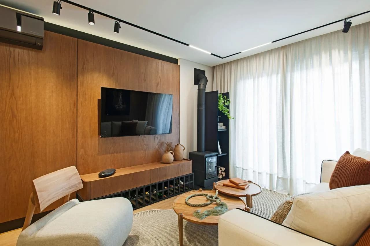 Sala de estar com painel de madeira, TV e cortina até o chão.