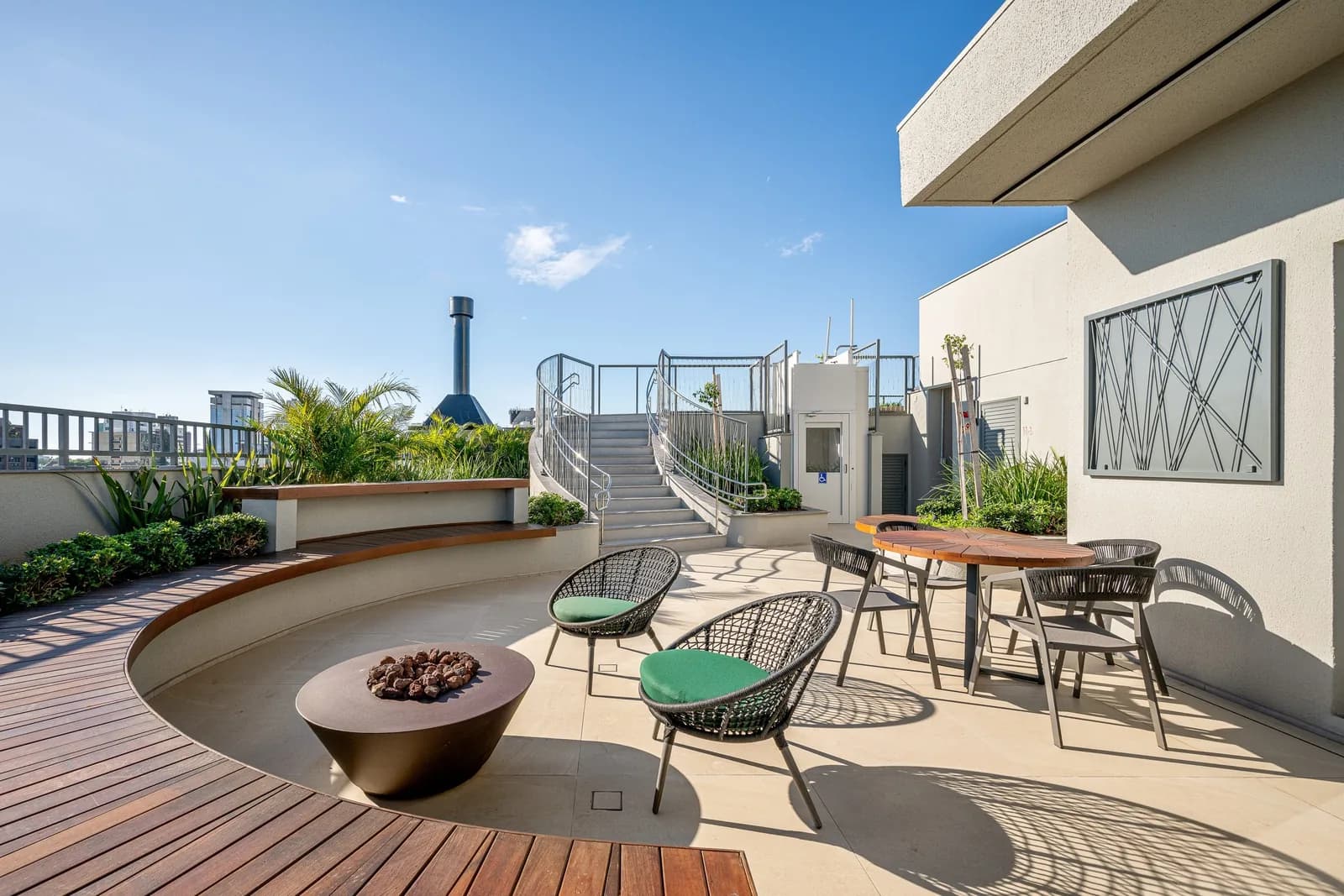 Lounge do rooftop com braseiro central, poltronas e deck de madeira.