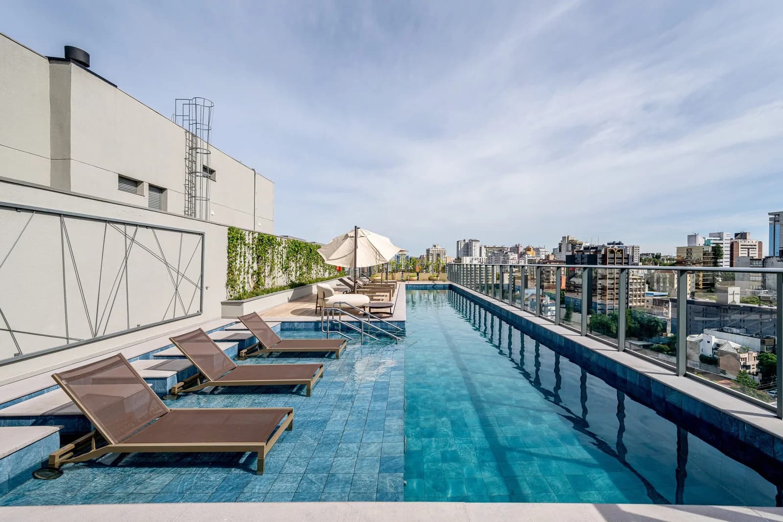 Piscina do rooftop, com espreguiçadeiras e vista para os prédios de Porto Alegre.