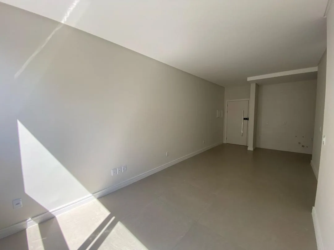 Sala vazia com piso porcelanato e porta de entrada ao fundo.