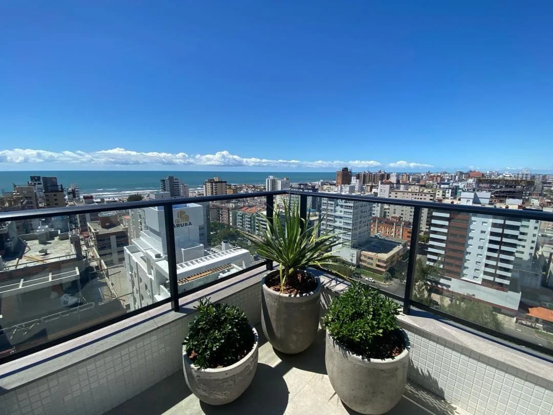 Sacada do rooftop com vasos de plantas e vista para o mar e a cidade.