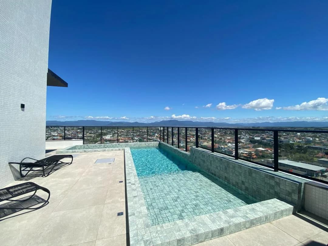 Piscina do rooftop com espreguiçadeiras e vista para a cidade e as montanhas.