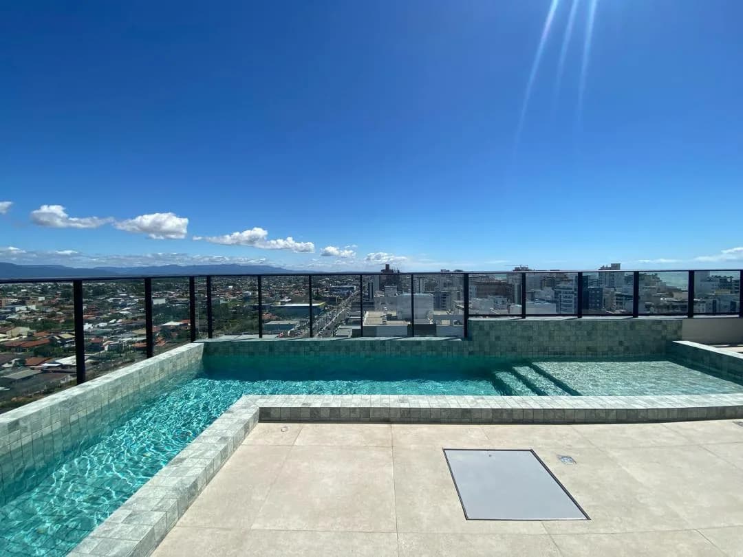 Piscina do rooftop com borda em pastilhas e vista aberta da cidade.